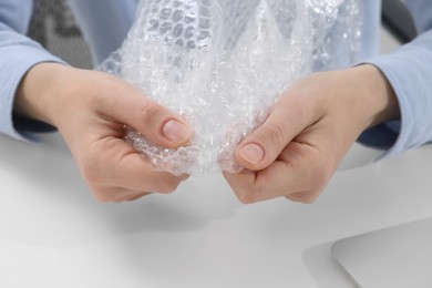 Woman popping bubble wrap at table in office, closeup. Stress relief