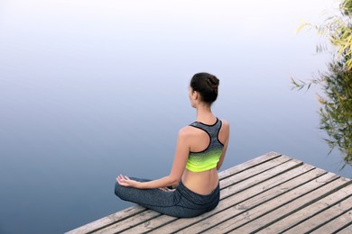 Photo of Woman meditating on wooden pier near river
