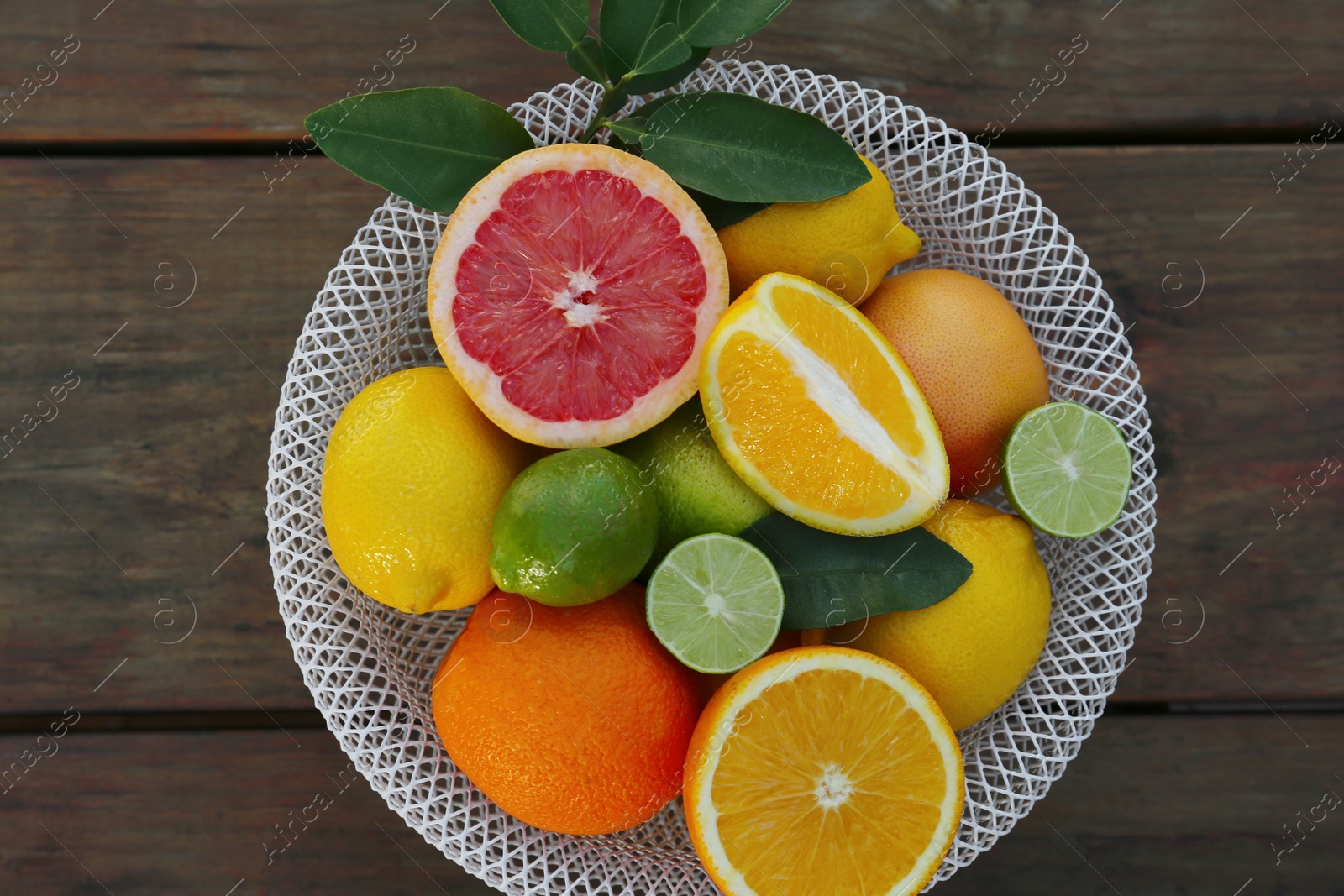 Photo of Bowl with different citrus fruits and leaves on wooden table, top view