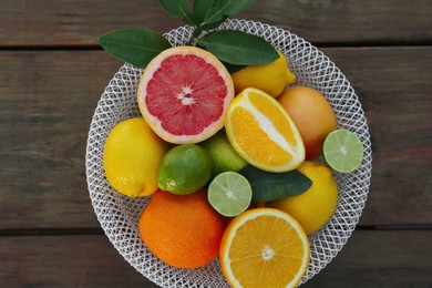 Bowl with different citrus fruits and leaves on wooden table, top view