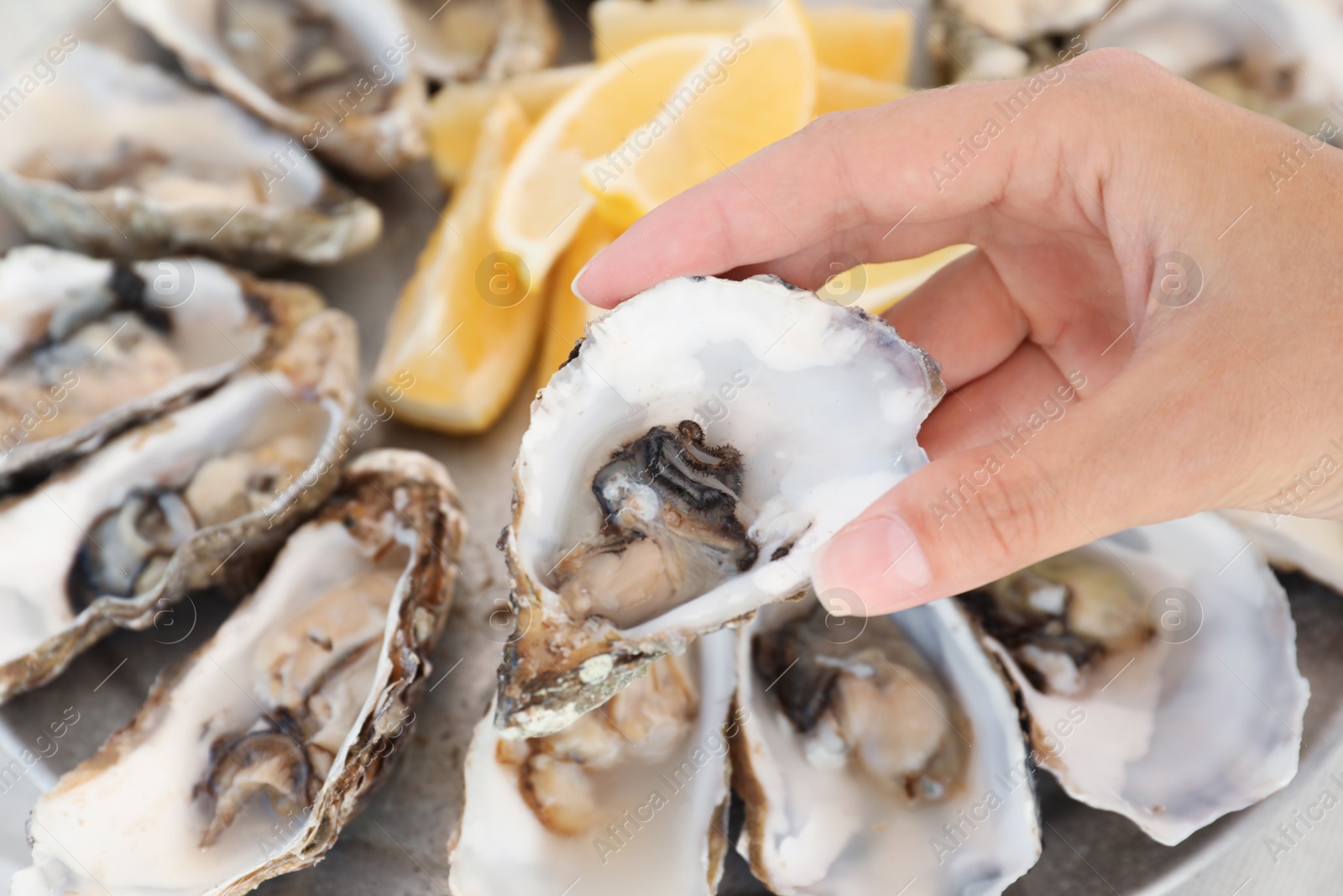 Photo of Woman holding fresh oyster over plate, focus on hand