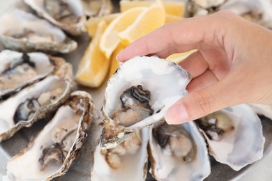 Woman holding fresh oyster over plate, focus on hand