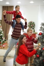 Photo of Mother and son decorating Christmas tree while father playing with daughter at home