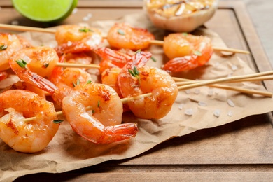 Photo of Skewers with delicious fried shrimps on wooden board, closeup