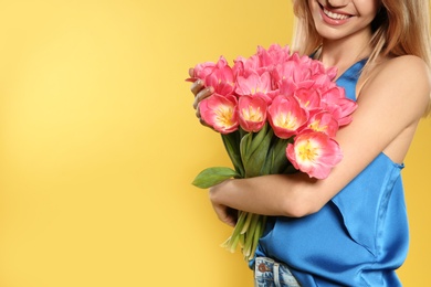 Photo of Beautiful girl holding spring tulips on yellow background, closeup with space for text. International Women's Day