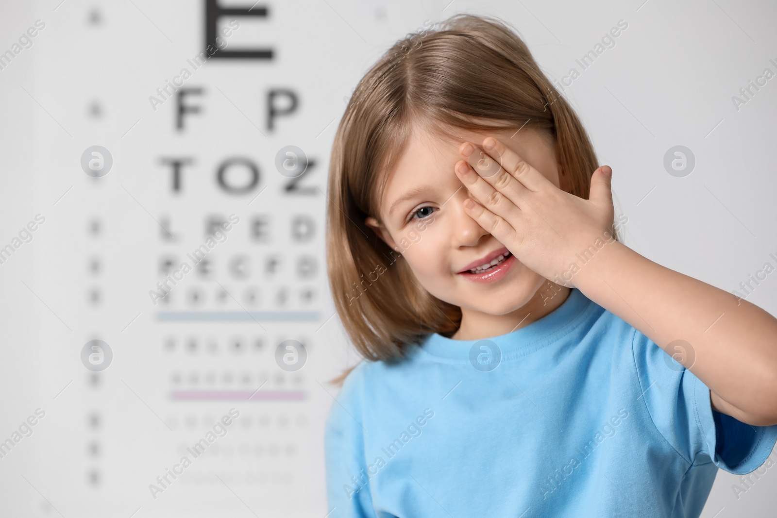 Photo of Little girl covering her eye against vision test chart