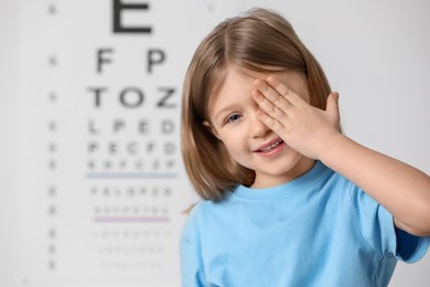 Little girl covering her eye against vision test chart