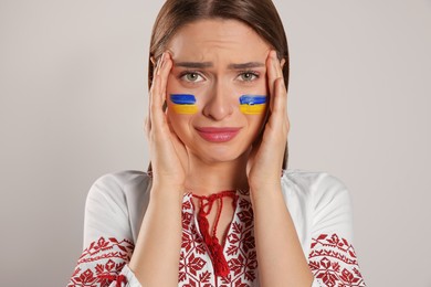 Photo of Sad young woman with drawings of Ukrainian flag on face against beige background