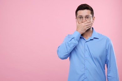 Photo of Embarrassed man covering mouth on pink background. Space for text