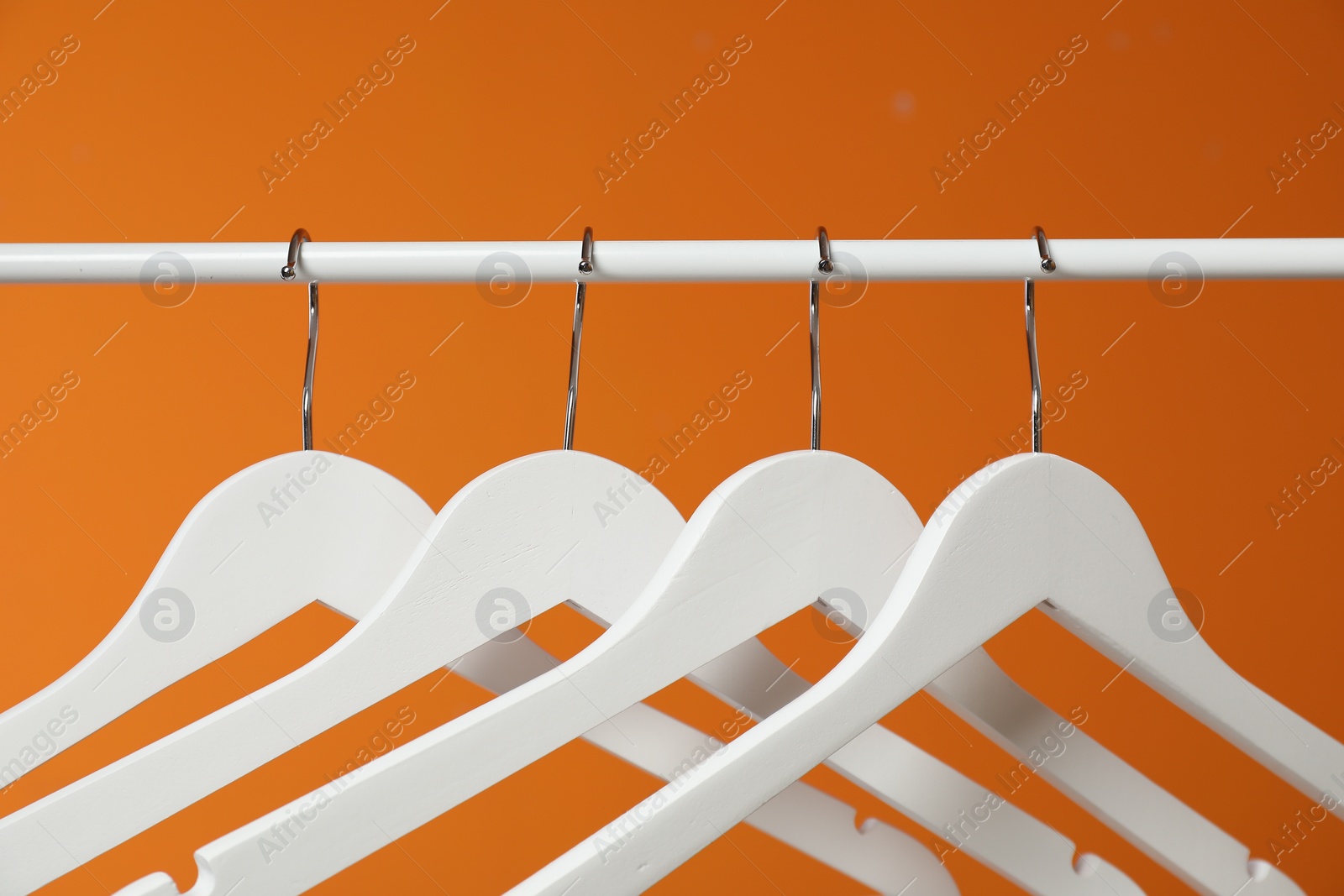 Photo of White clothes hangers on rack against orange background, closeup