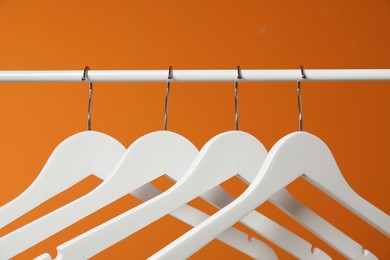 Photo of White clothes hangers on rack against orange background, closeup