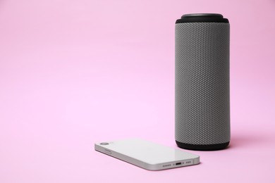 Portable bluetooth speaker and smartphone on pink background, space for text. Audio equipment