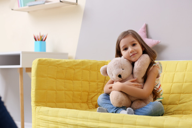 Photo of Cute little girl sitting on sofa at home