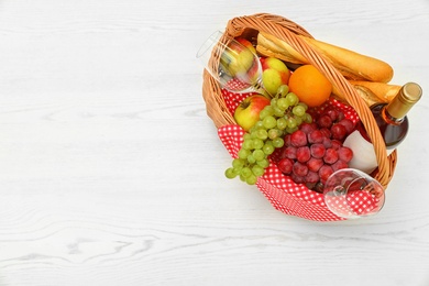 Photo of Picnic basket with products and wine on white wooden table, top view. Space for text