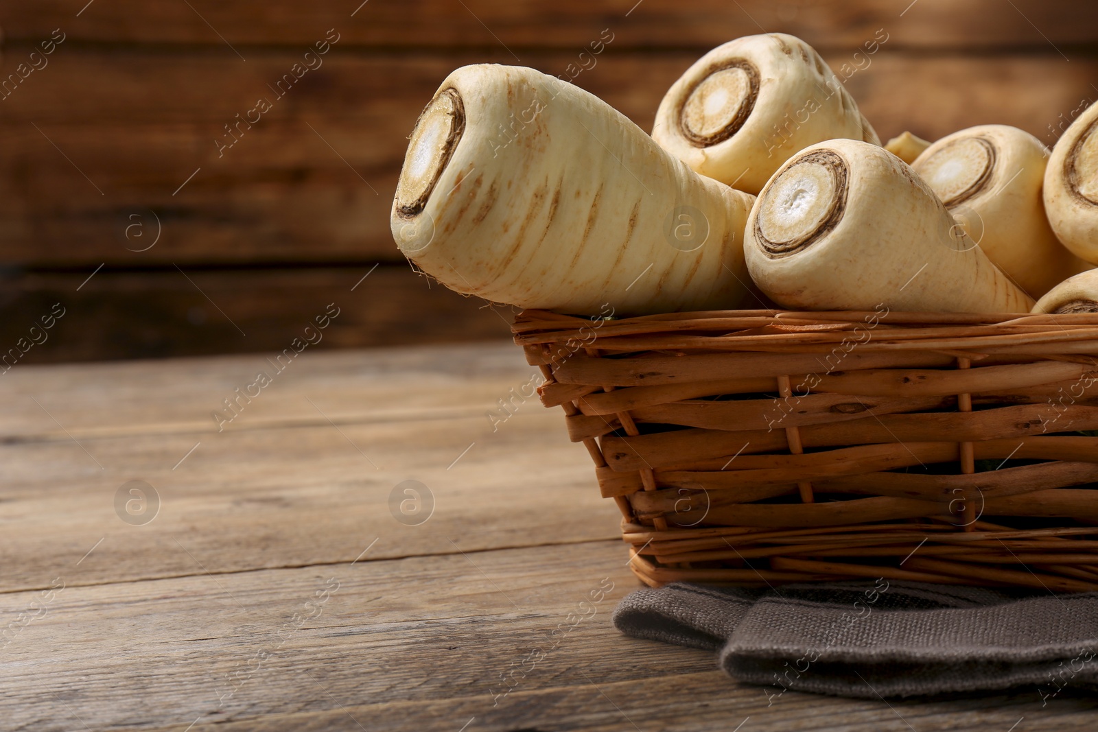 Photo of Wicker basket with delicious fresh ripe parsnips on wooden table, closeup. Space for text