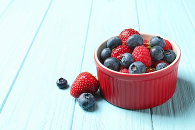 Photo of Bowl with raspberries, strawberries and blueberries on wooden table