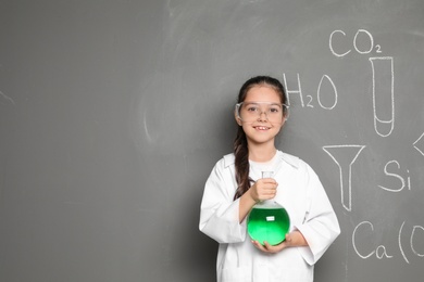 Photo of Little school child in laboratory uniform with flask of liquid and chemical formulas on grey background