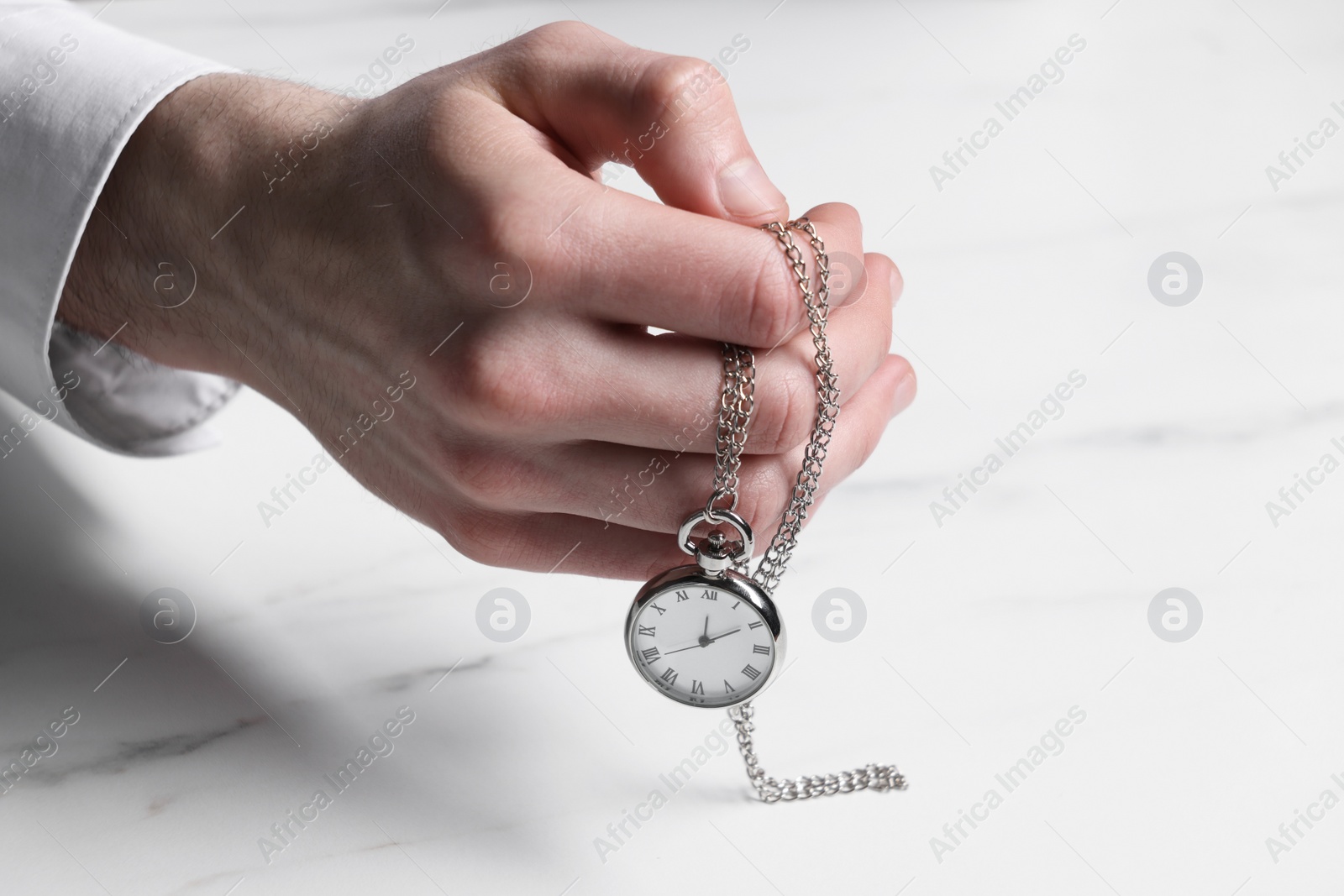 Photo of Man holding chain with elegant pocket watch at white marble table, closeup