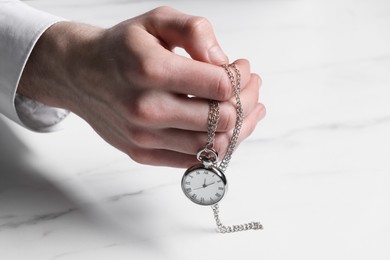 Photo of Man holding chain with elegant pocket watch at white marble table, closeup