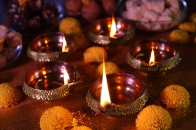 Photo of Diwali celebration. Diya lamps and chrysanthemum flowers on shiny table, closeup