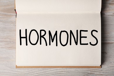 Photo of Notebook with word HORMONES on white wooden table, top view