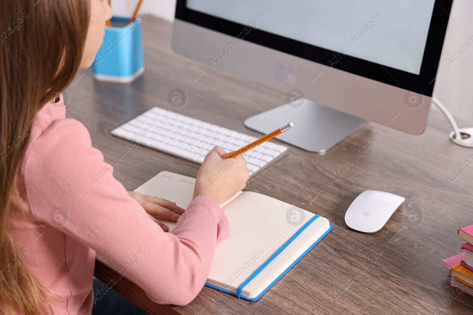 Photo of E-learning. Girl taking notes during online lesson at table indoors, closeup