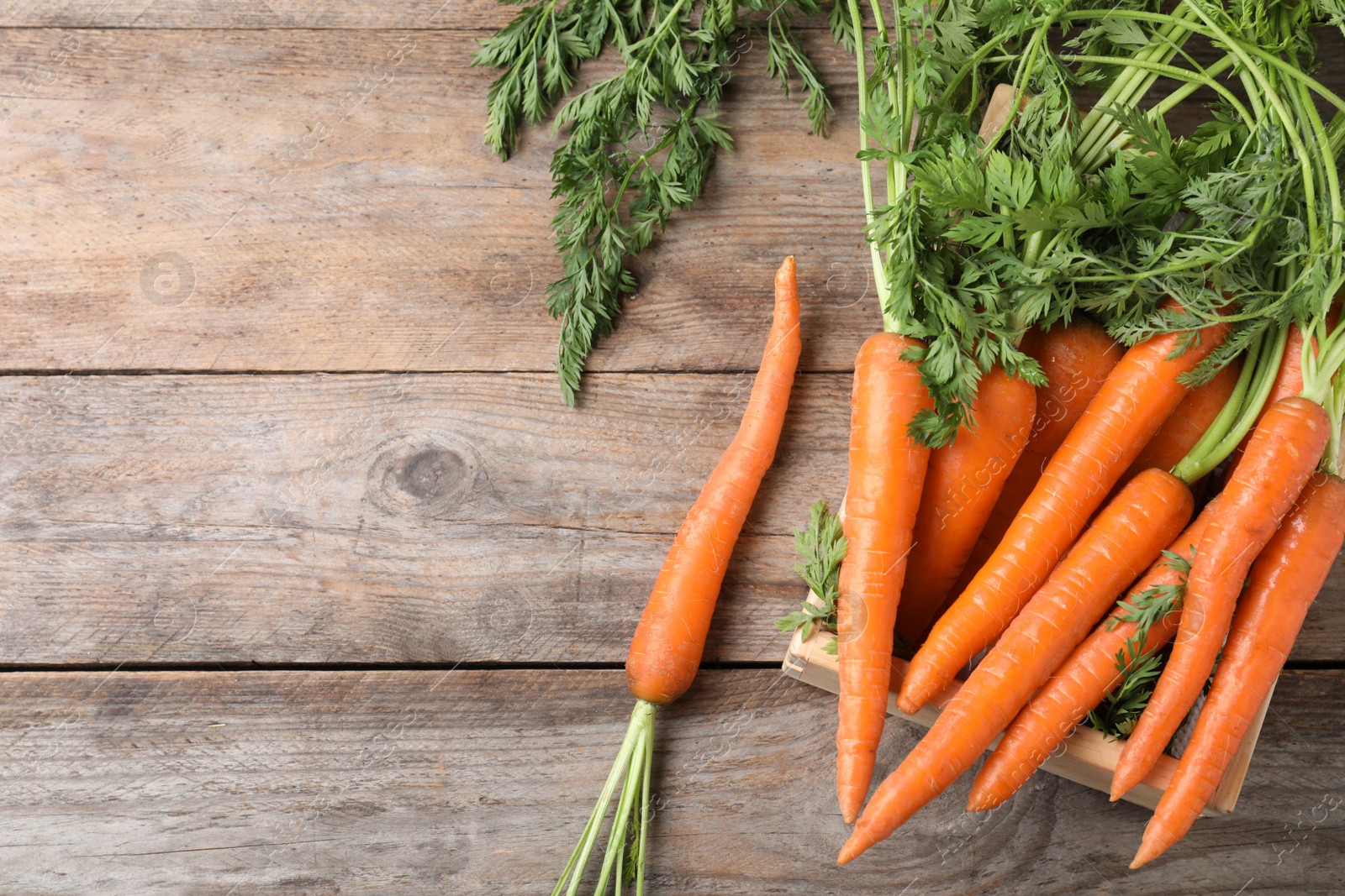 Photo of Crate of fresh carrots on wooden background, top view. Space for text