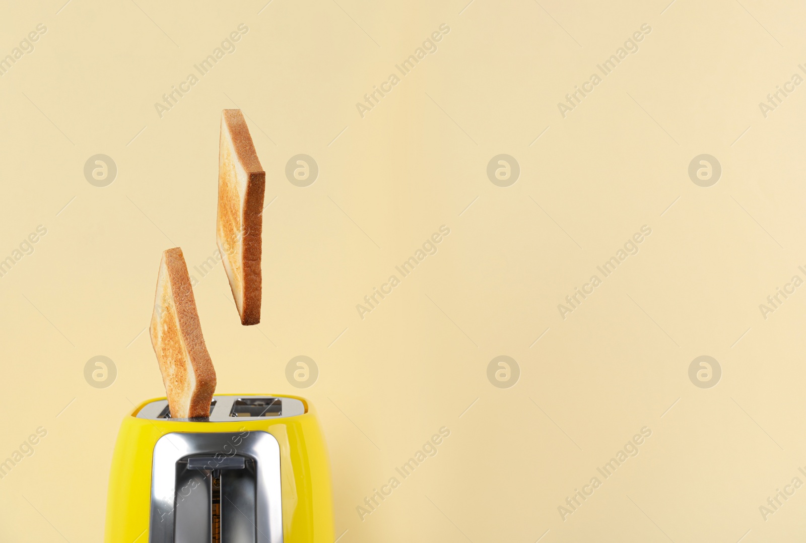 Photo of Bread slices popping up from modern toaster on beige background, closeup. Space for text