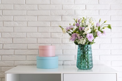 Photo of Bouquet of beautiful Eustoma flowers on cabinet near white brick wall. Space for text
