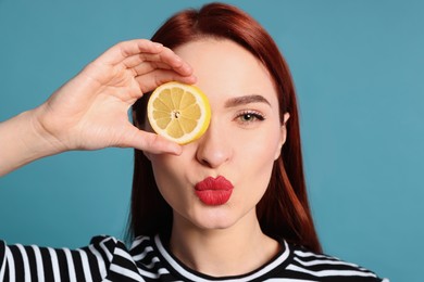 Photo of Beautiful redhead woman covering eye with lemon and blowing kiss on light blue background