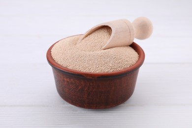 Bowl and scoop with active dry yeast on white wooden table