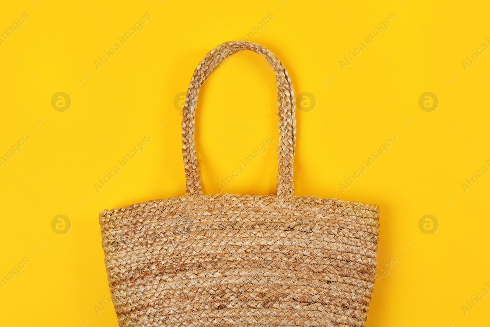 Photo of Stylish woman's straw bag on yellow background, top view