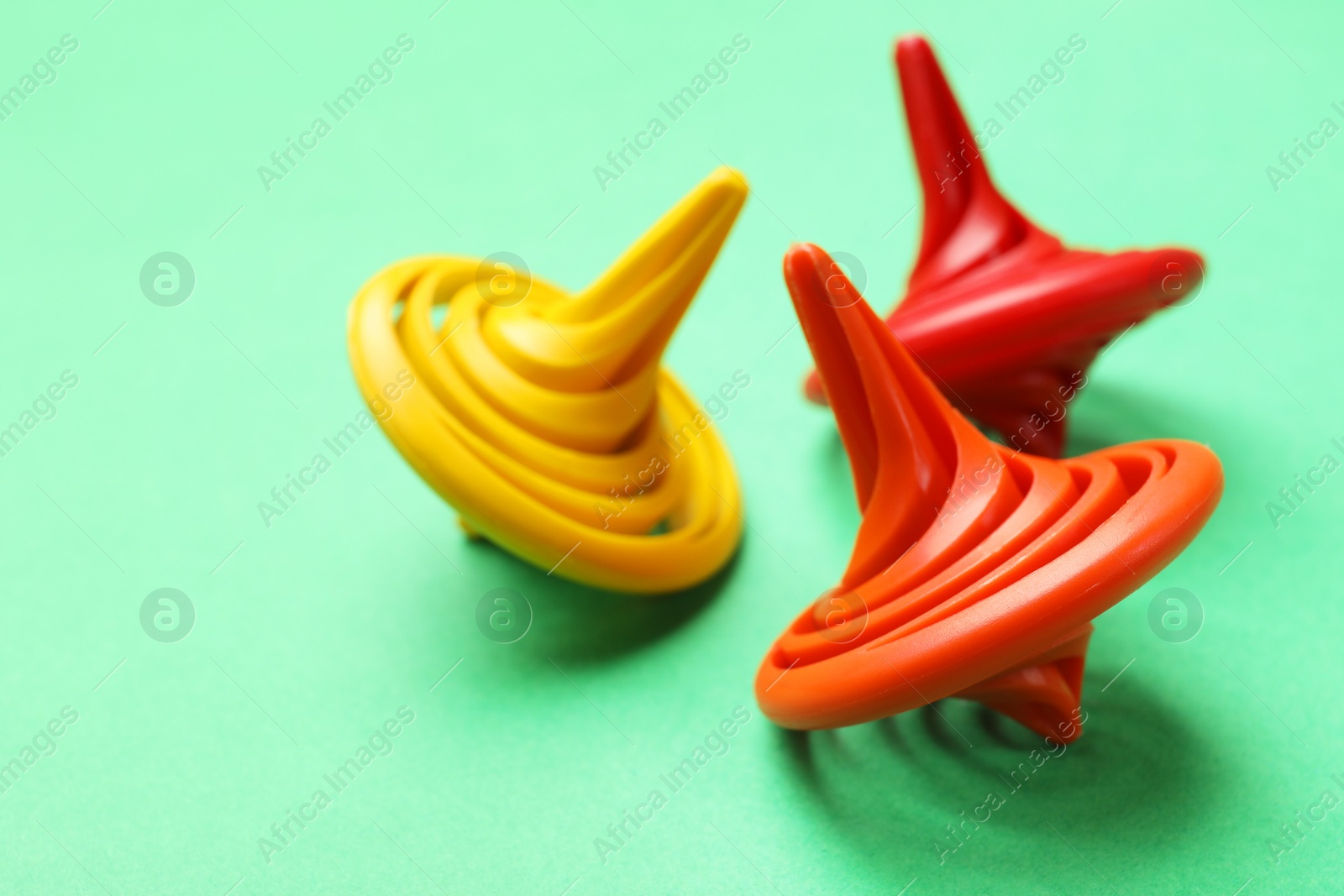 Photo of Many colorful spinning tops on green background, closeup. Space for text