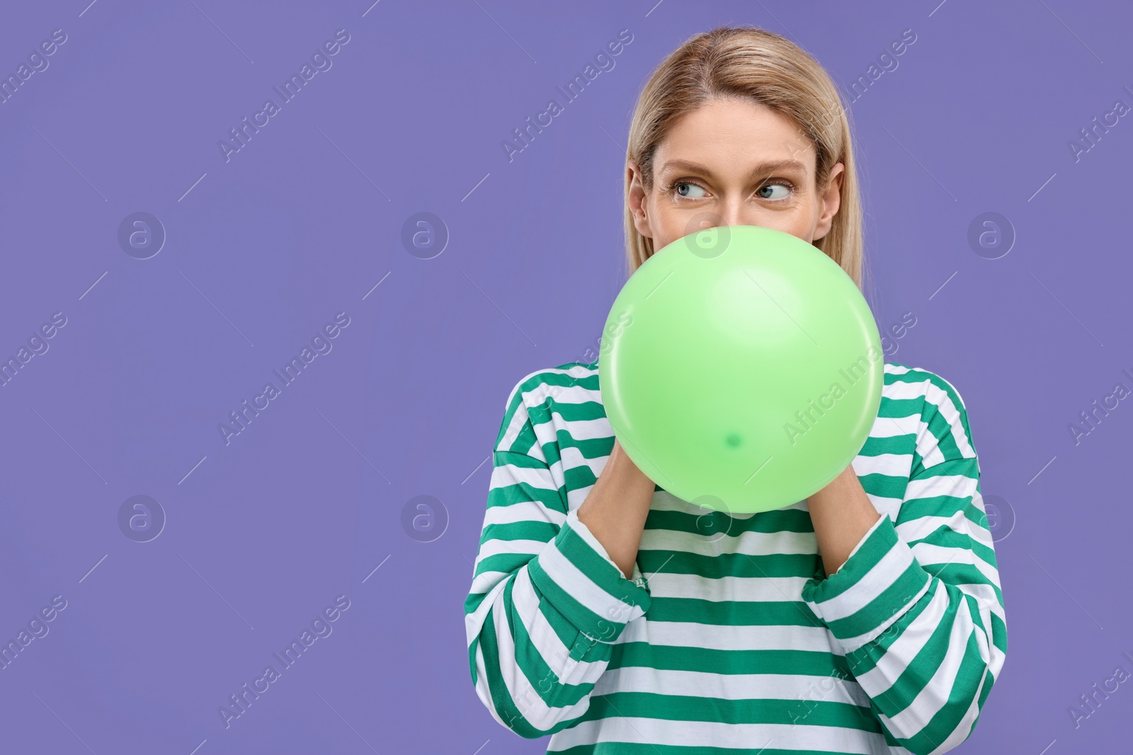 Photo of Woman blowing up balloon on violet background. Space for text