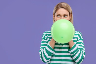 Photo of Woman blowing up balloon on violet background. Space for text