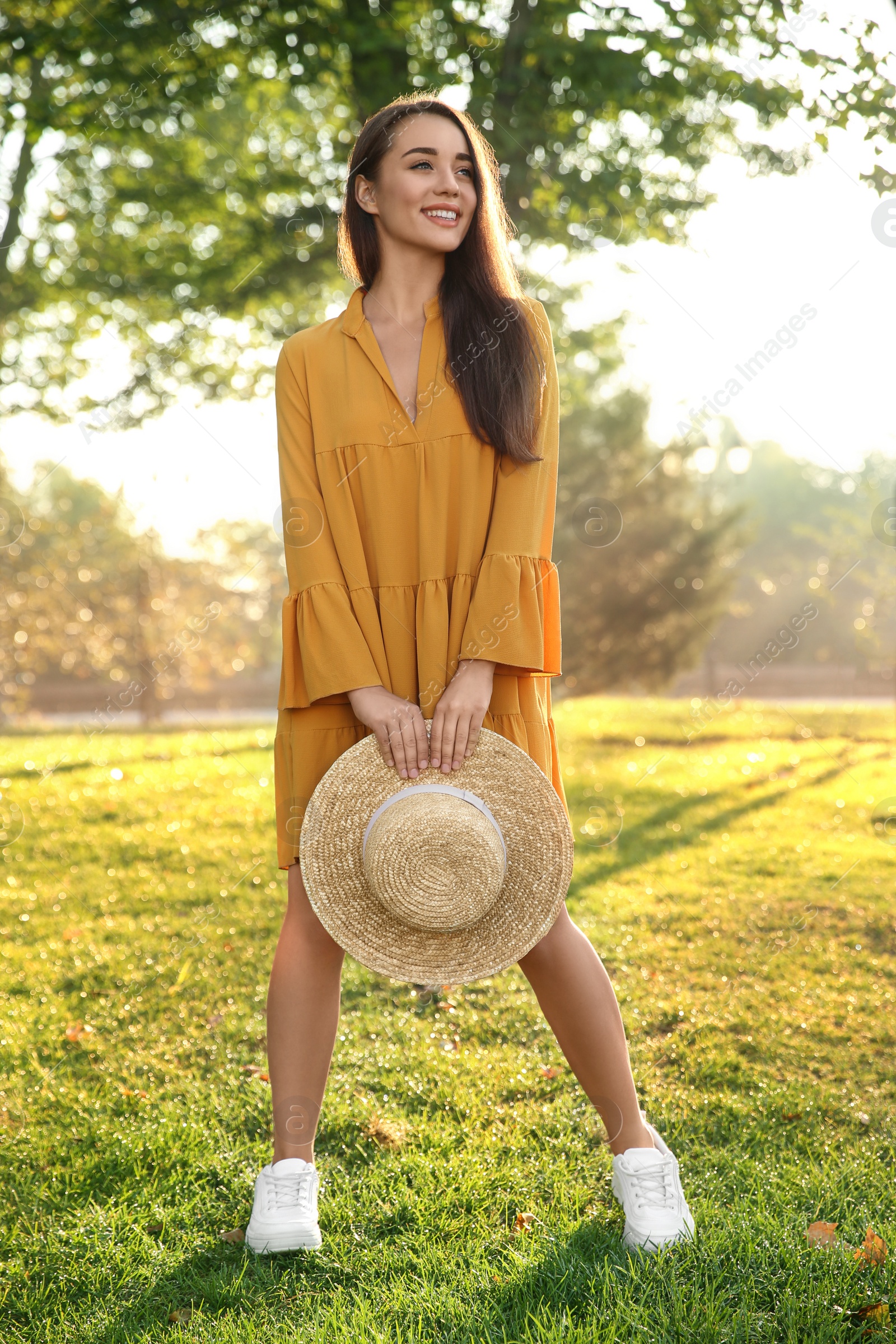 Photo of Beautiful young woman wearing stylish yellow dress with straw hat in park