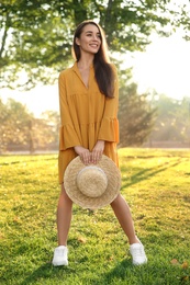 Photo of Beautiful young woman wearing stylish yellow dress with straw hat in park