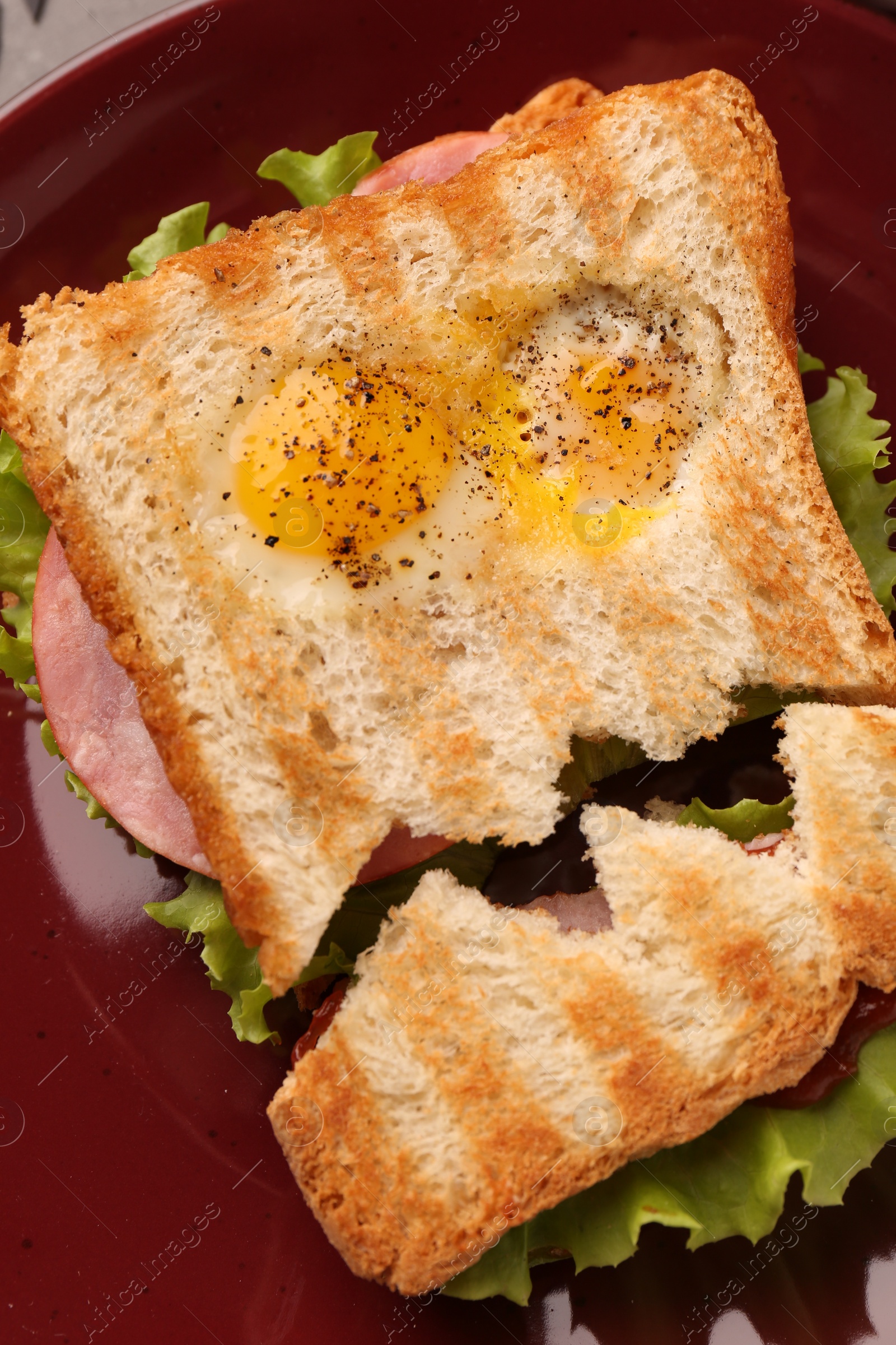 Photo of Cute monster sandwich with fried eggs on burgundy plate, top view. Halloween snack