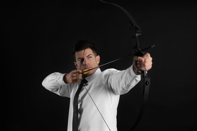 Businessman with bow and arrow practicing archery on black background