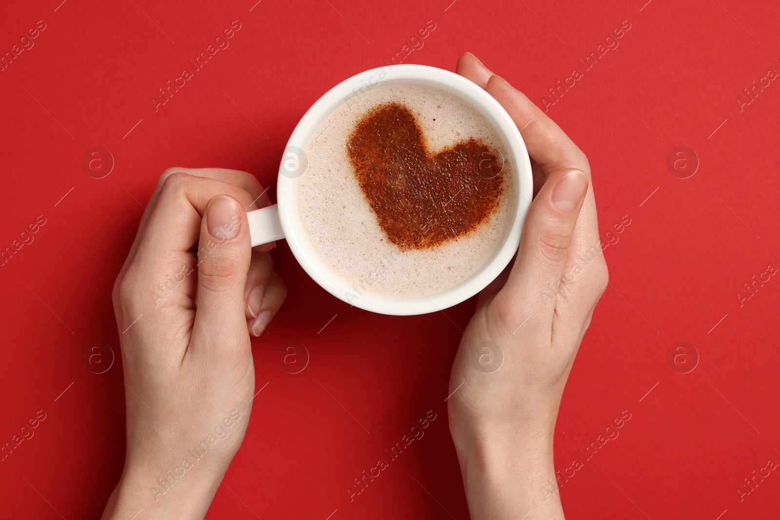 Photo of Woman holding cup of aromatic coffee with heart shaped decoration on red background, top view