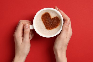 Photo of Woman holding cup of aromatic coffee with heart shaped decoration on red background, top view