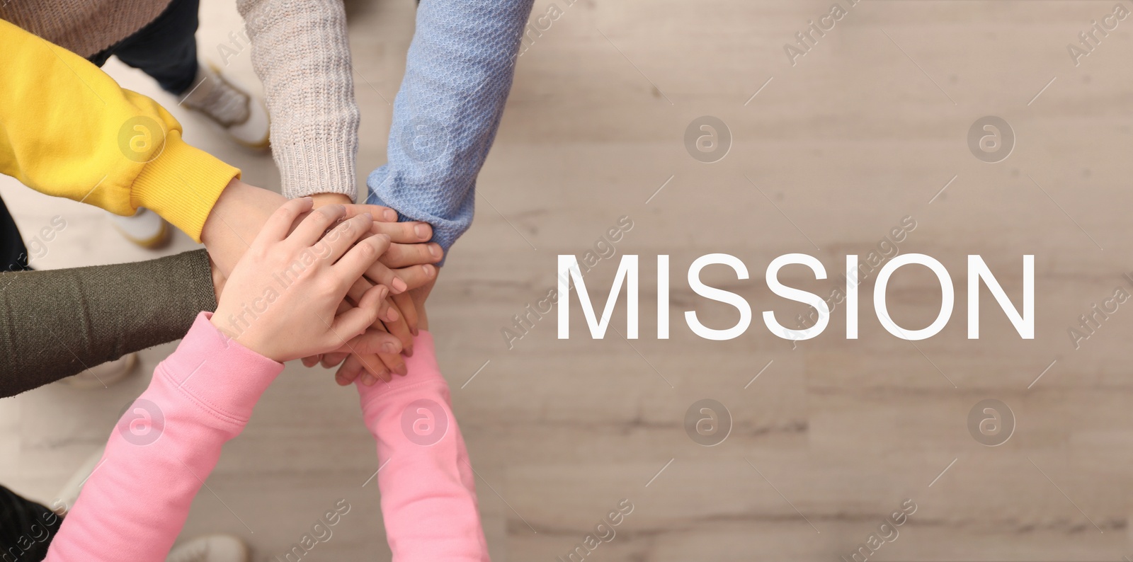 Image of People holding hands together over wooden background and text MISSION, top view. Banner design
