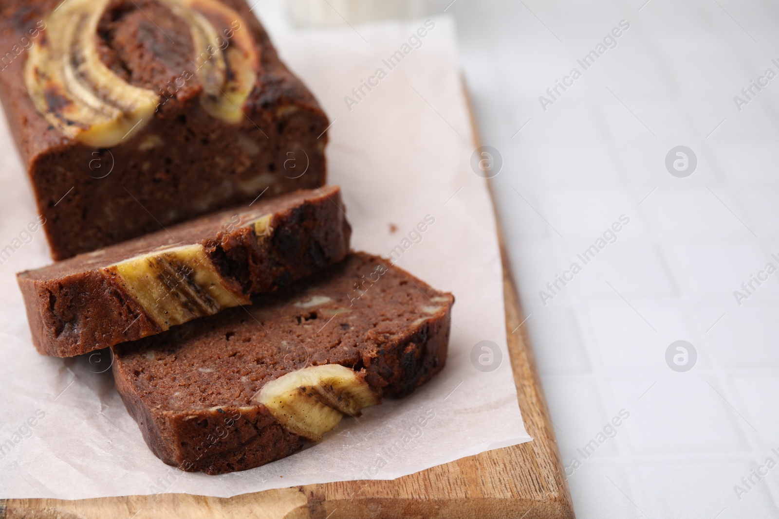Photo of Delicious banana bread on white tiled table, closeup. Space for text