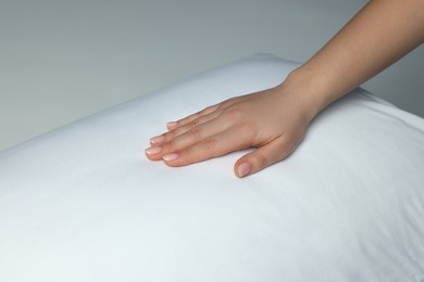 Woman touching soft white pillow on bed, closeup