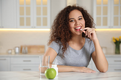 African-American woman taking vitamin pill in kitchen