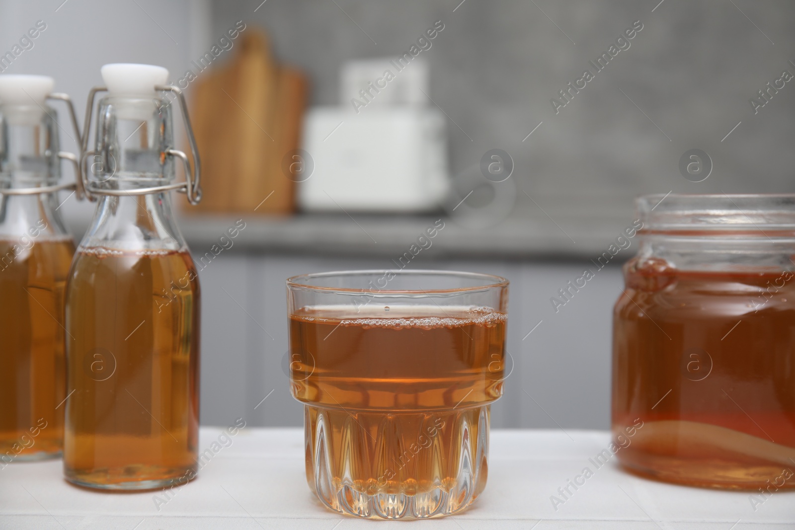 Photo of Homemade fermented kombucha in glass, jar and bottles on white table in kitchen