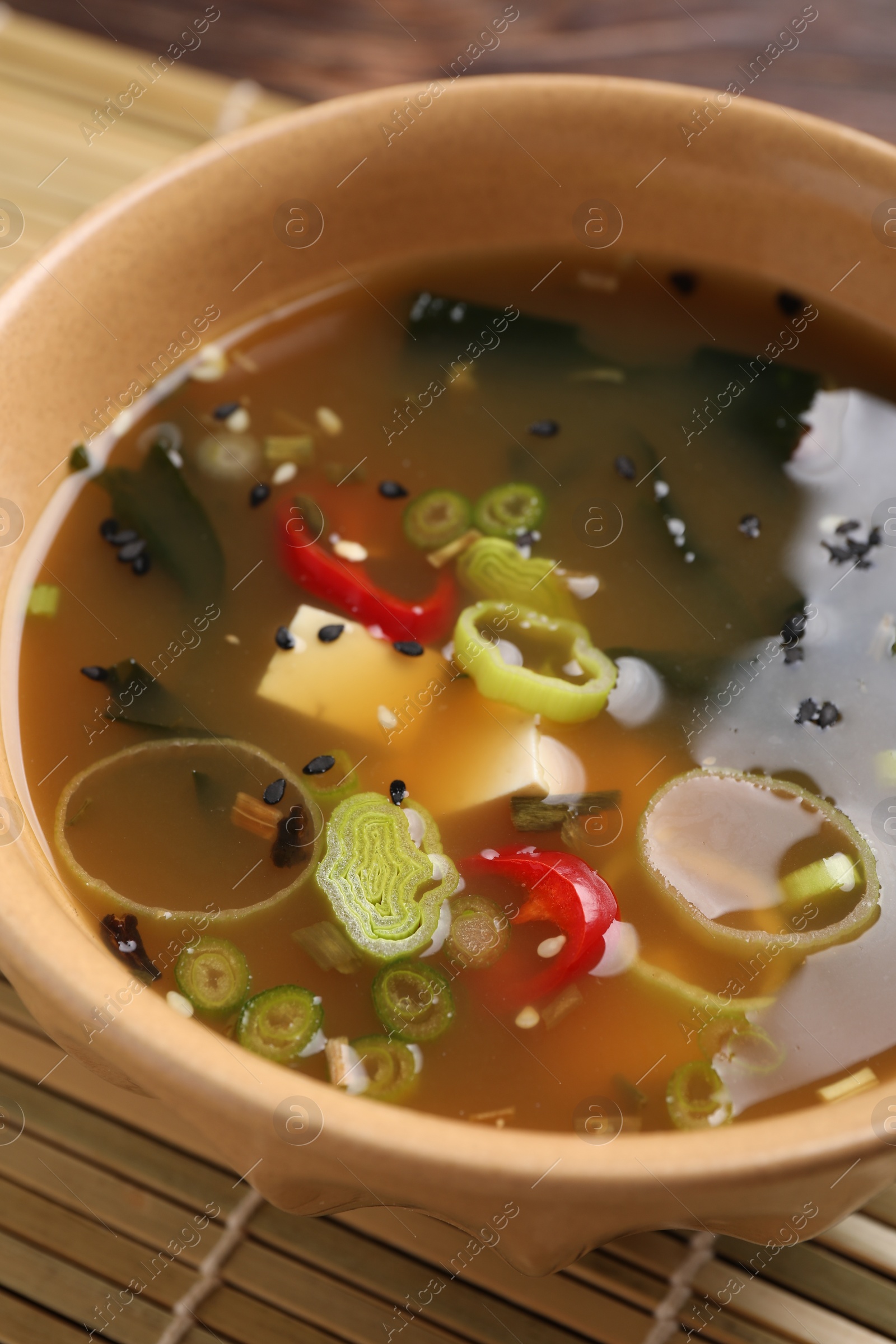 Photo of Bowl of delicious miso soup with tofu on bamboo mat, closeup