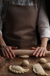 Woman rolling dough for chebureki on wooden table, closeup