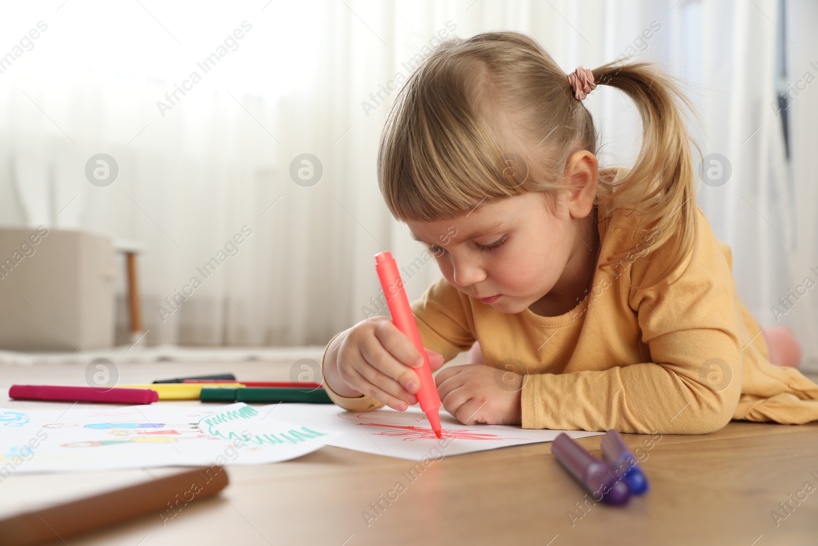 Photo of Cute little girl drawing with marker on floor indoors. Child`s art