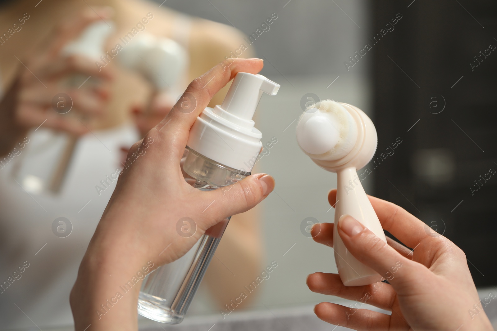 Photo of Washing face. Woman applying cleansing foam onto brush near mirror in bathroom, closeup